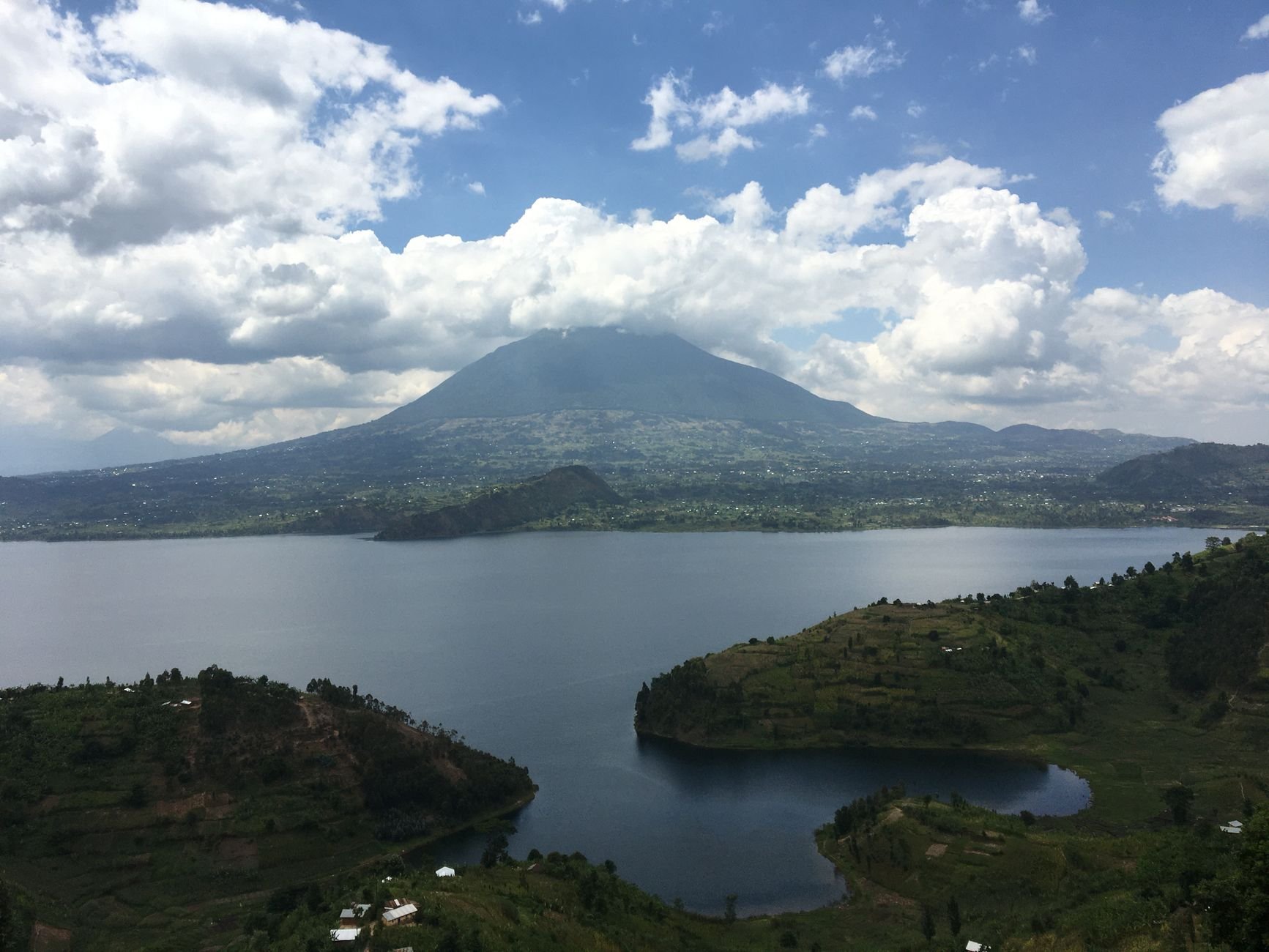 A still mountain lake surrounded by green hills, with clouds overhead.