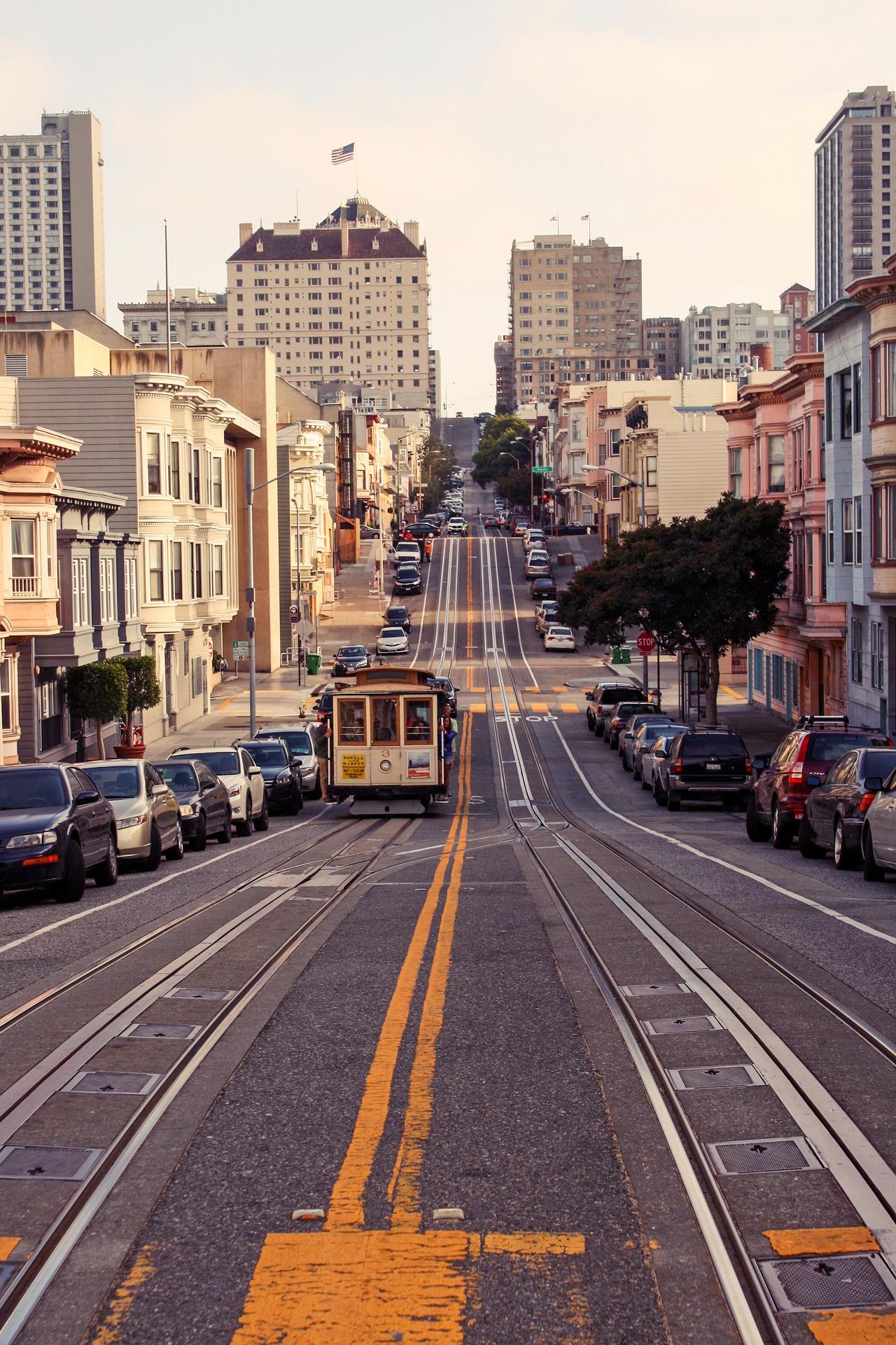 A cable car climbs a steep San Francisco street lined with parked cars and hillside buildings
