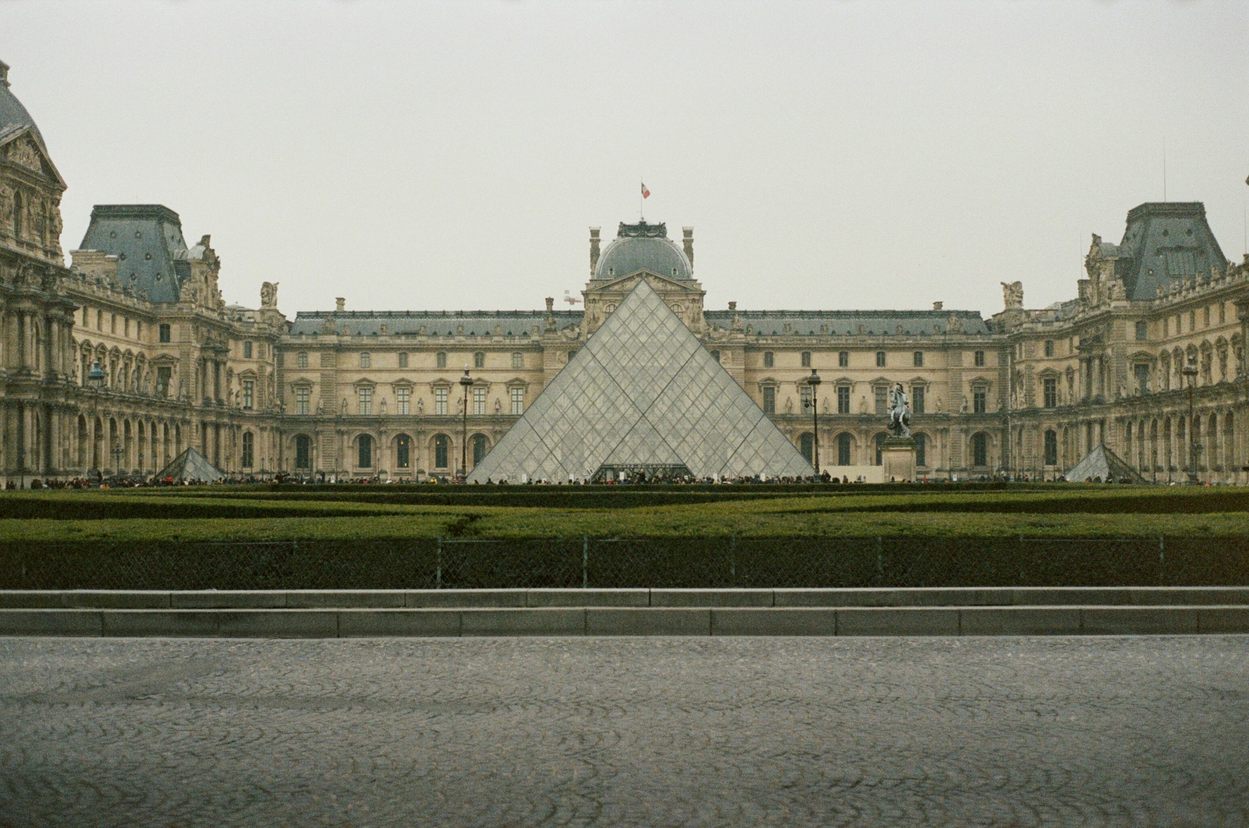 The Louvre Museum with its glass pyramid on a cloudy day.