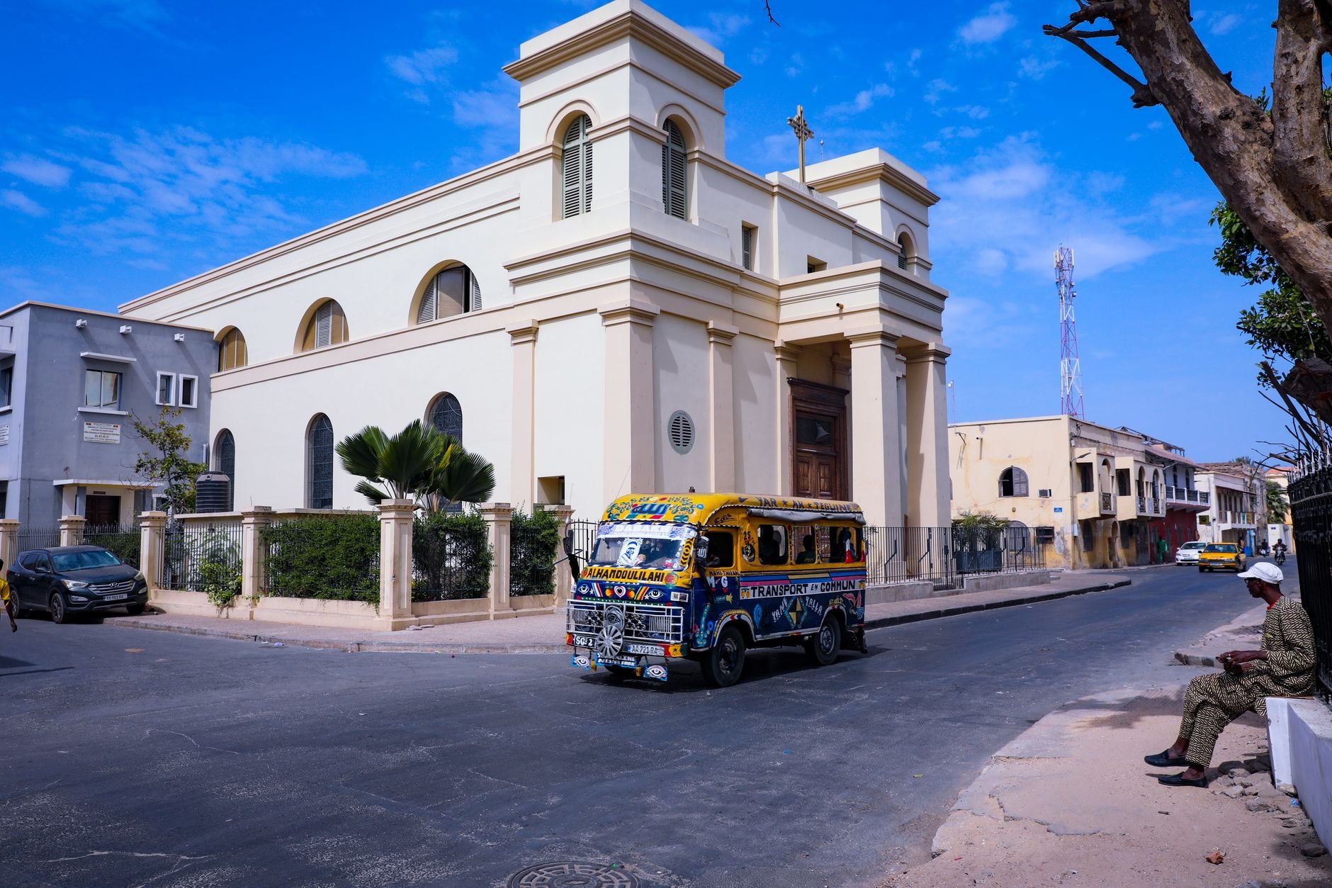 A brightly painted minibus passing a historic church on a city street.