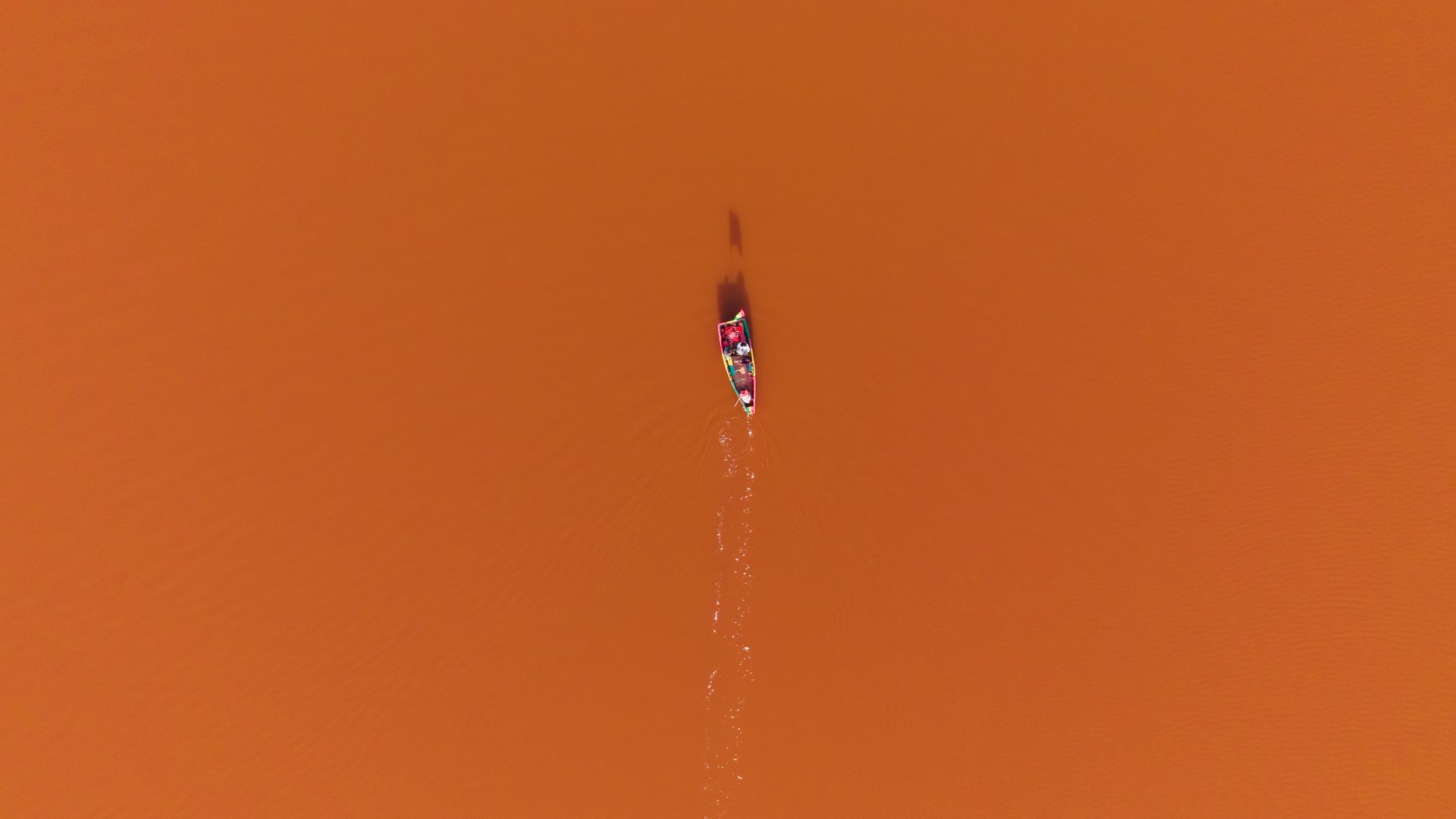 Aerial view of a canoe crossing a pink-tinted lake.