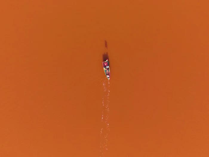 Aerial view of a canoe crossing a pink-tinted lake.