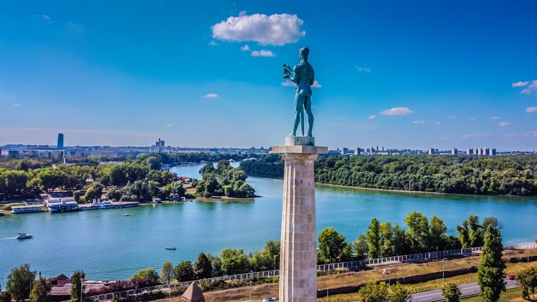 A statue on a hilltop monument overlooks a river confluence and city skyline.
