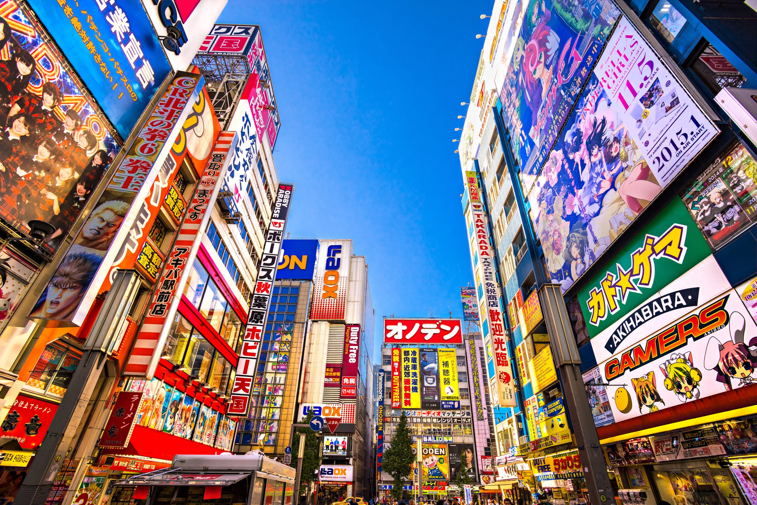 Neon signs and billboards cover high-rise buildings along a narrow city street in Tokyo