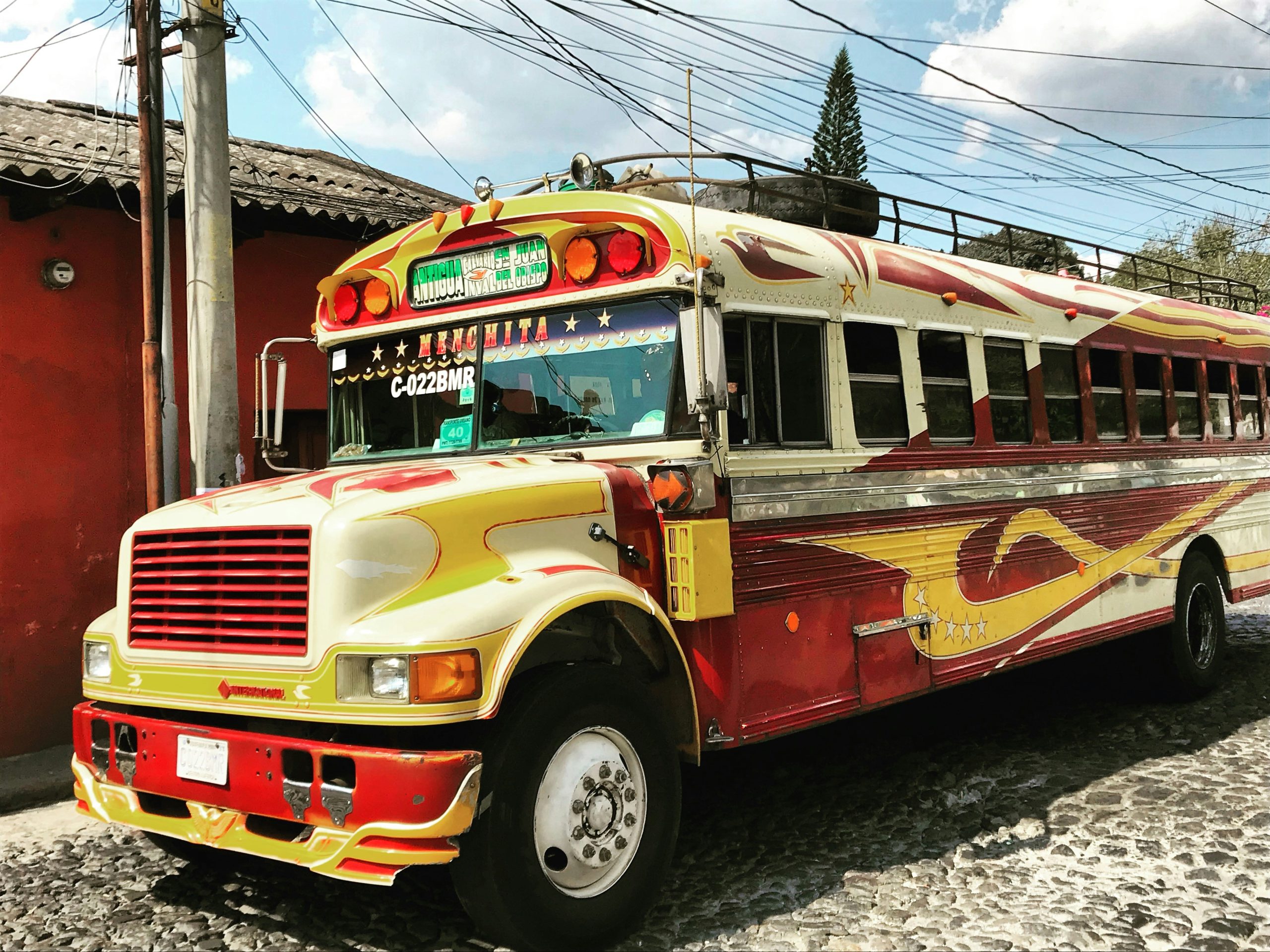 A retired school bus repainted in red, cream and gold with chrome trim, parked on a cobbled street.