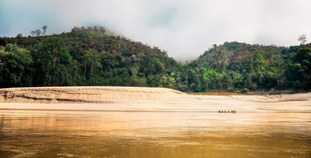 Small boat on a river with lush green hills and misty sky in the background.