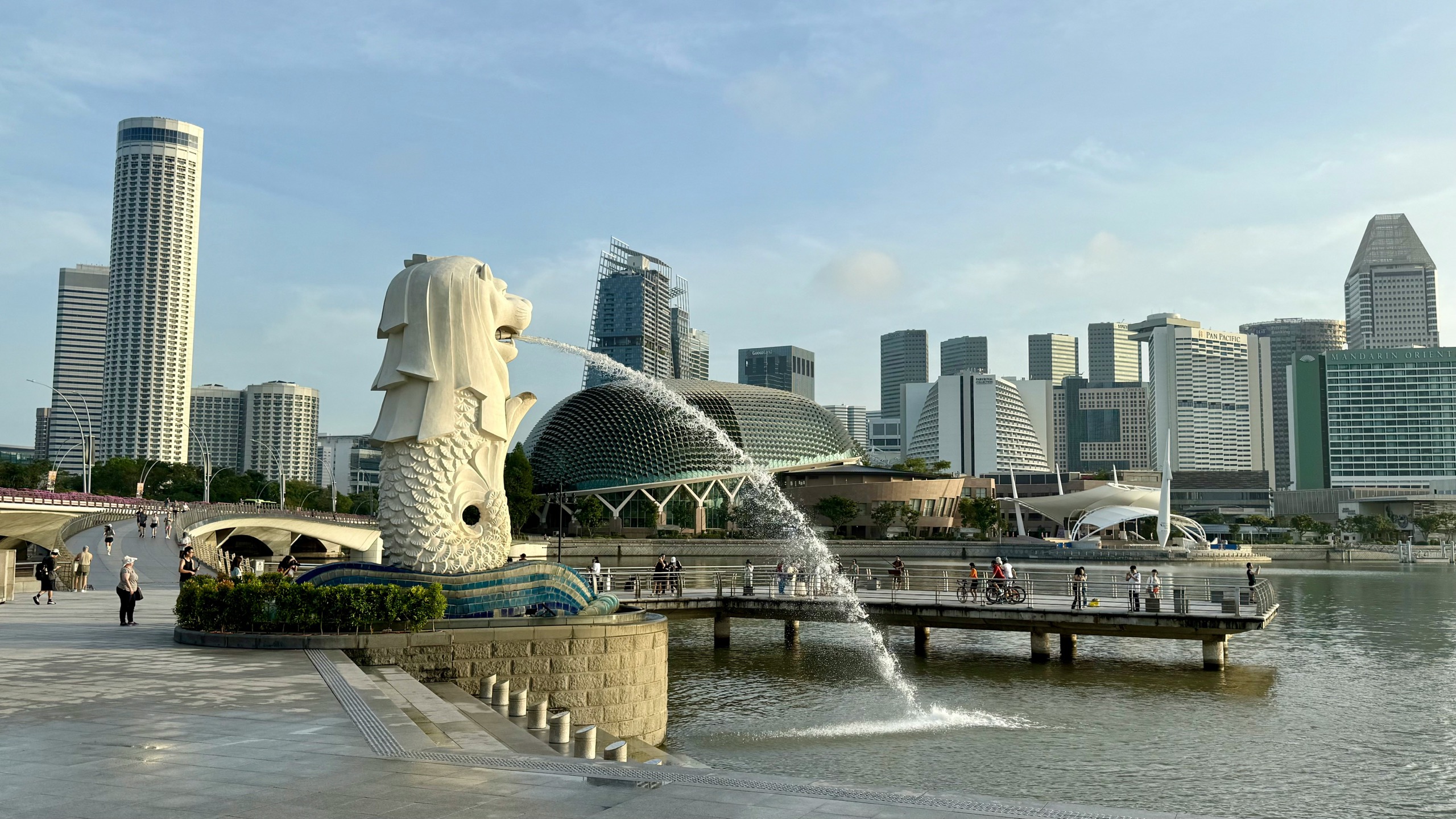 The Merlion statue spouts water into Marina Bay in front of the Esplanade theatres and the towers of the central business district under a clear morning sky.