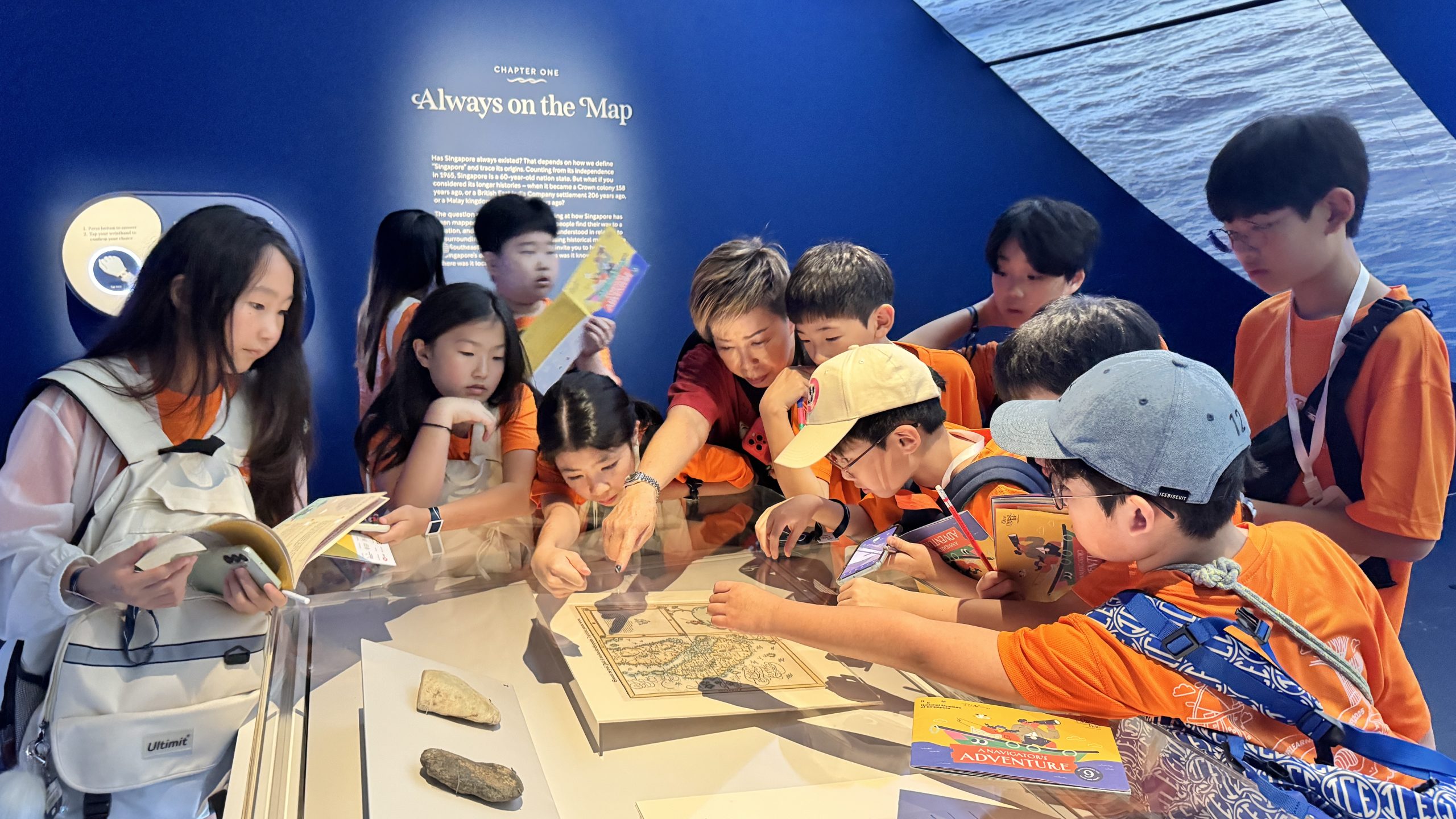 Students gather around a display case examining a historical map exhibit in a museum