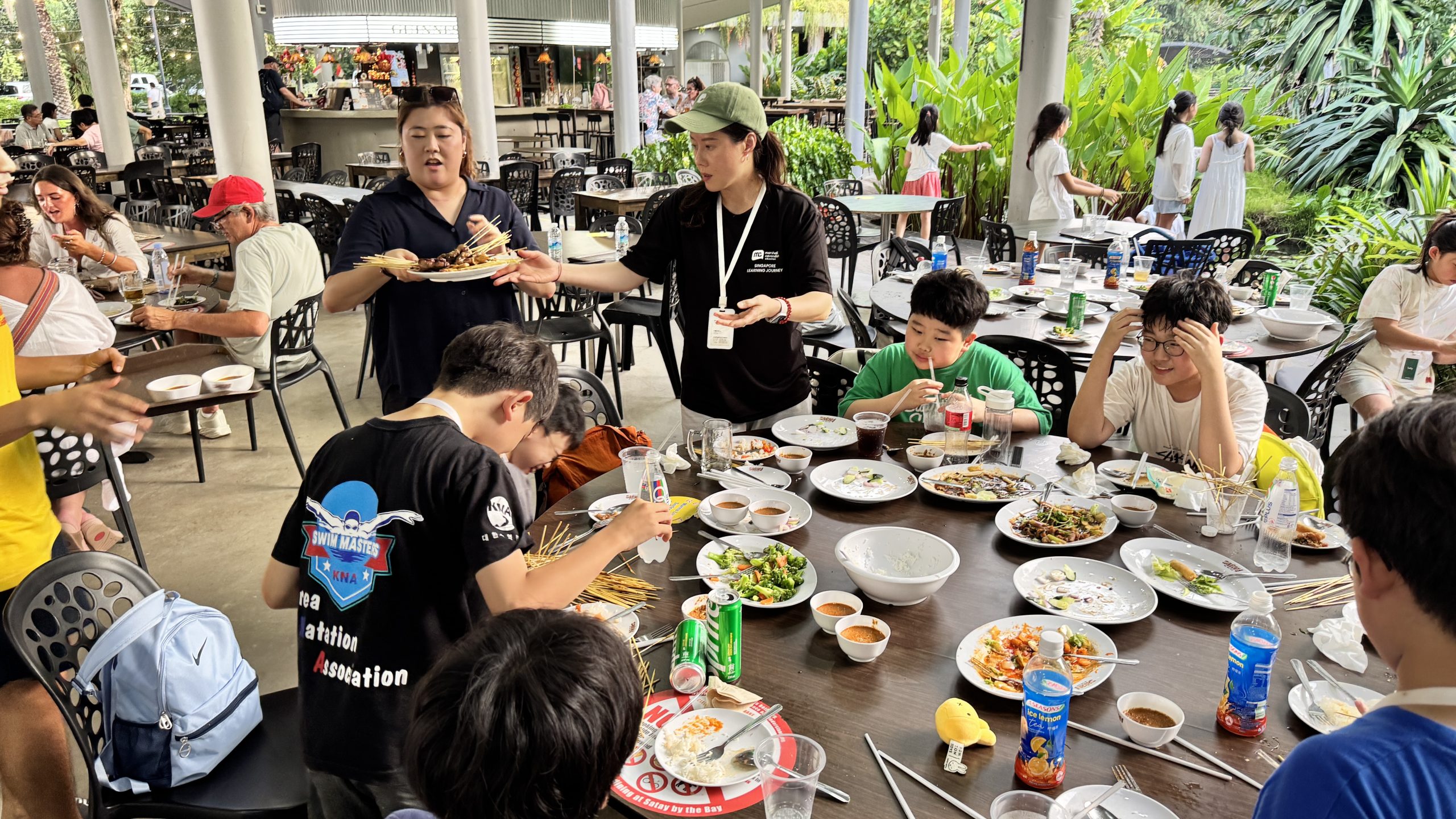 Students share a meal at a long outdoor table lined with shared dishes