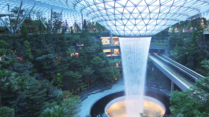 Teen travelers pause beneath the latticed glass dome as an indoor waterfall cascades through the lush atrium at Jewel Changi