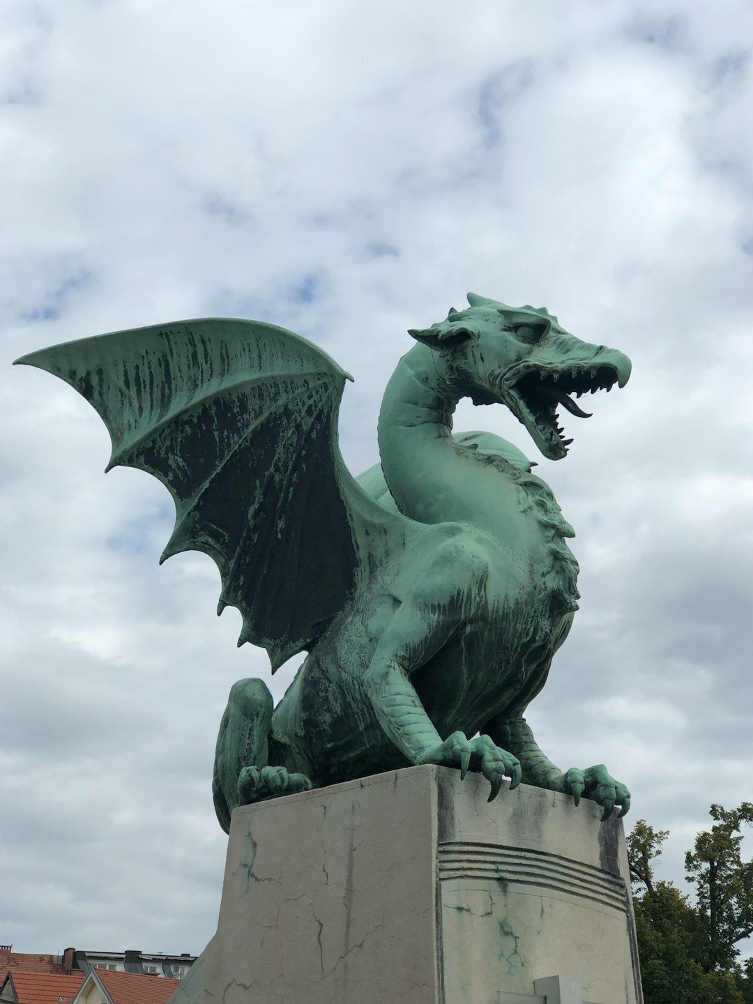 A green dragon statue standing on a stone pedestal on a bridge.