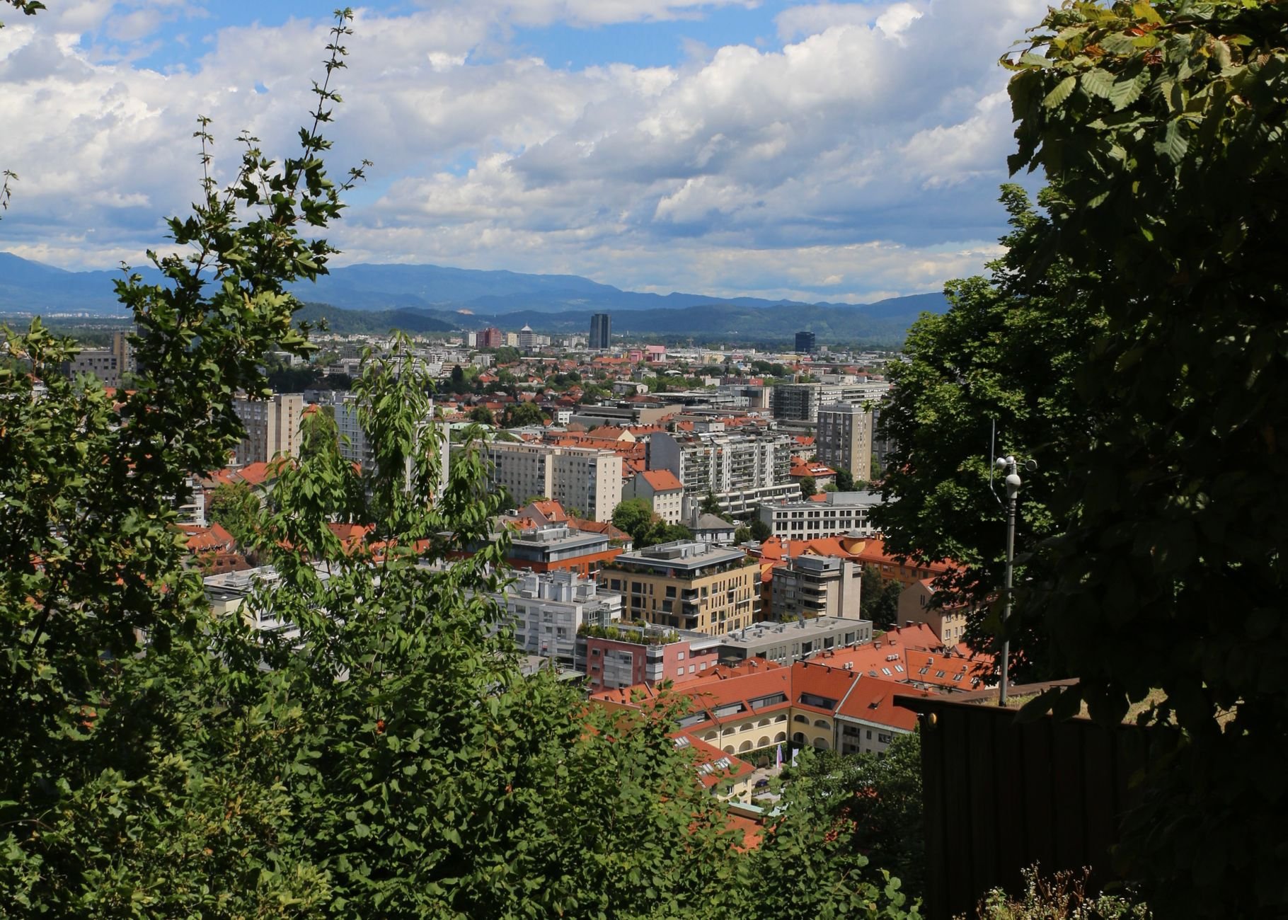 A panoramic view of a riverside city with a hilltop castle above red-roofed buildings.