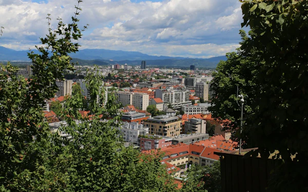 A panoramic view of a riverside city with a hilltop castle above red-roofed buildings.