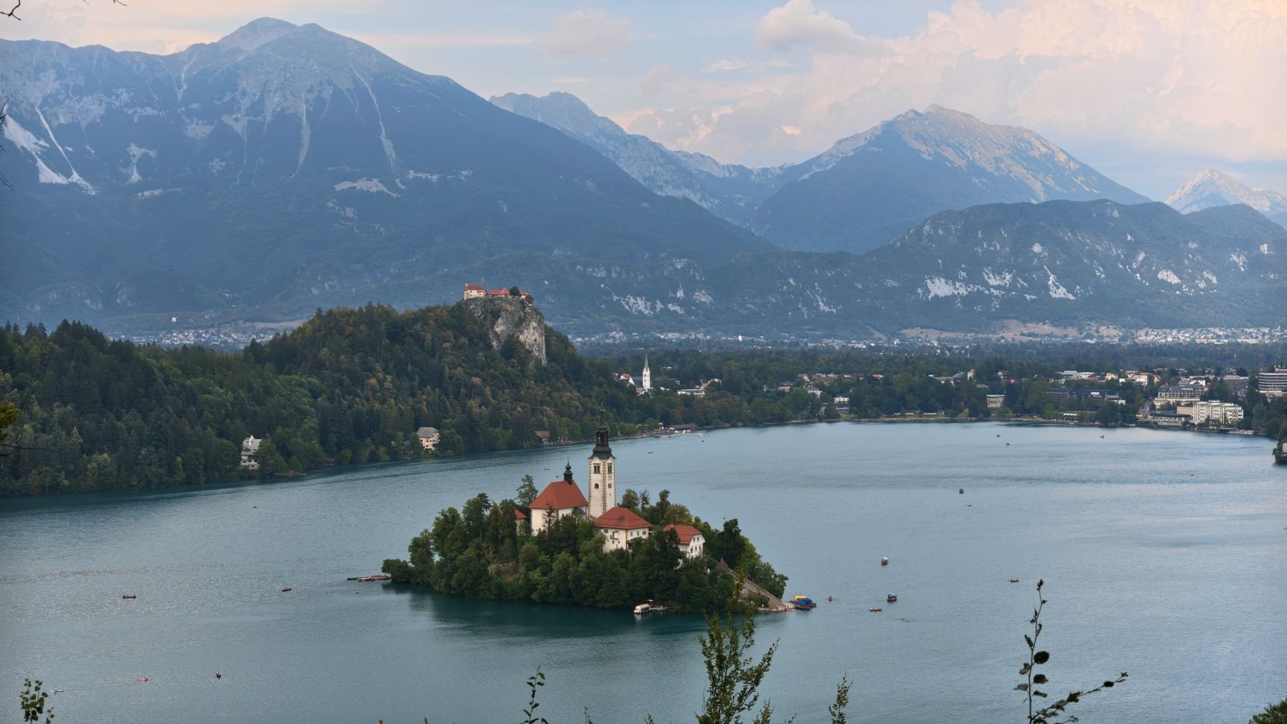 A calm alpine lake with a small church on an island, framed by forested mountains.
