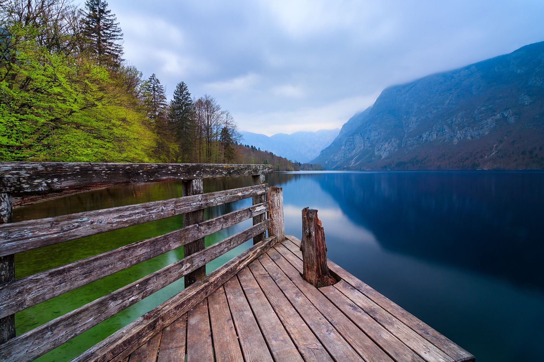 A wooden pier extending into a still lake, with green mountains rising beyond it.