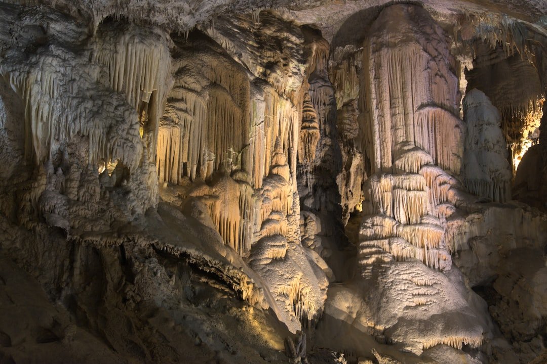 A small group of visitors standing inside an illuminated limestone cave chamber.