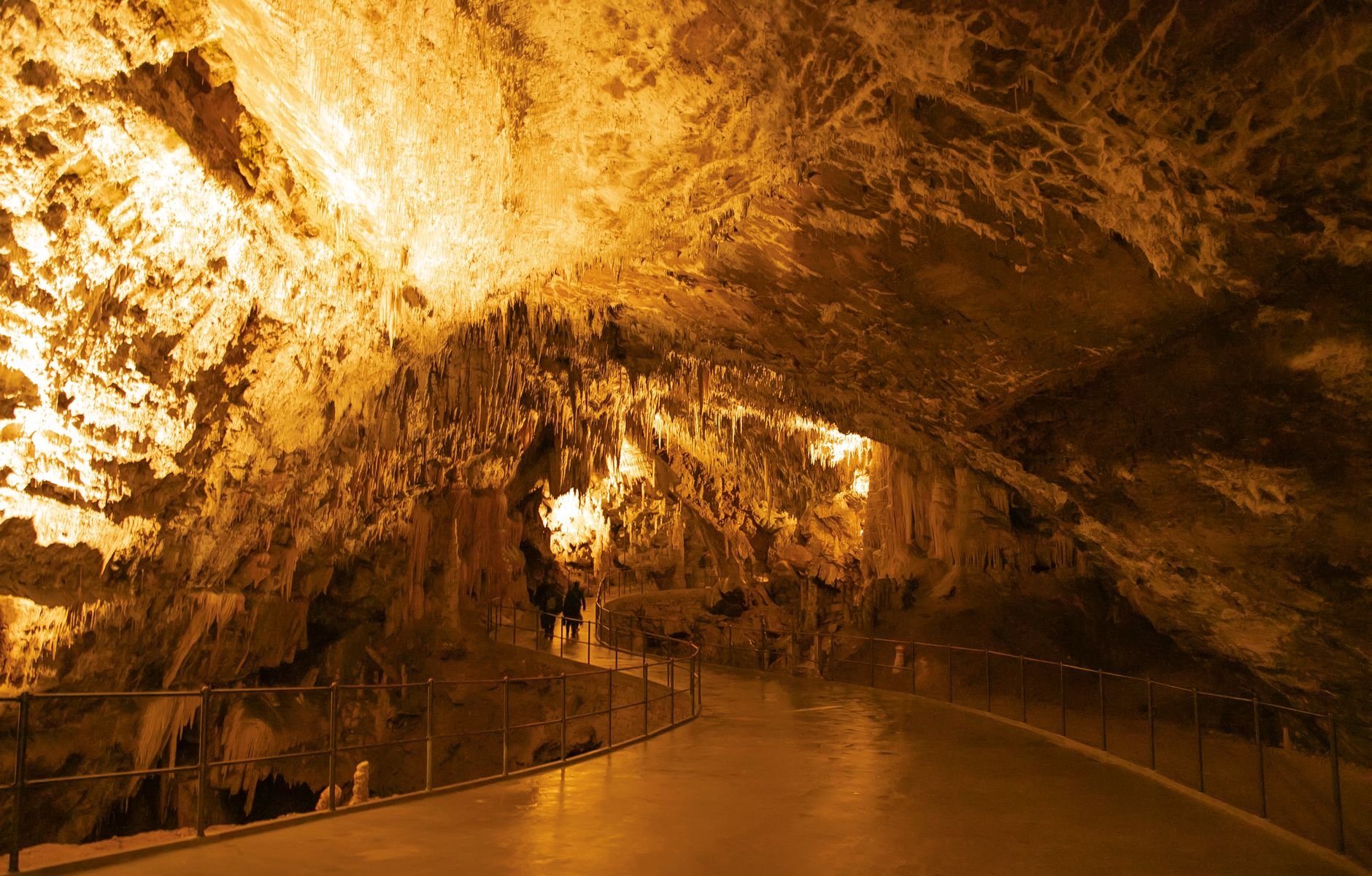 Illuminated stalactite and stalagmite formations inside an underground cave chamber.