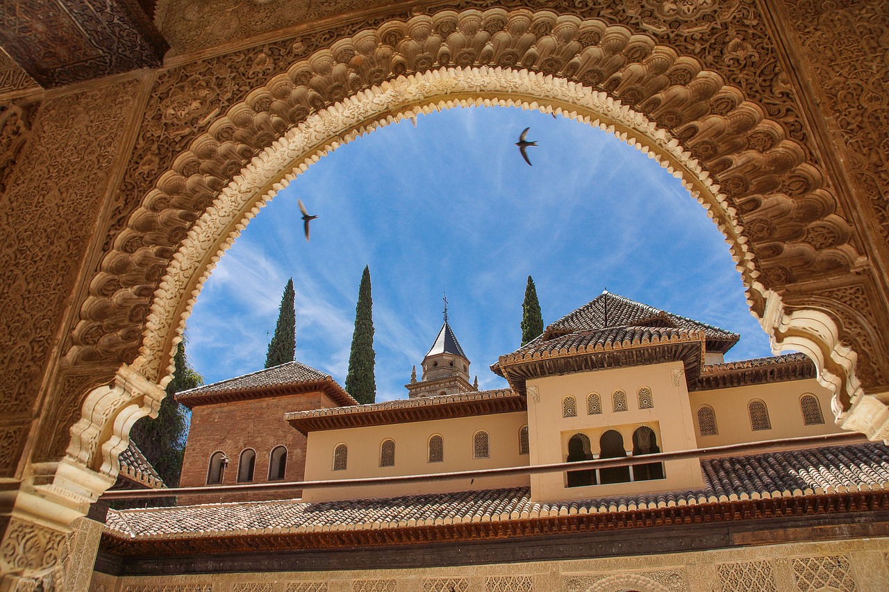 Birds fly over a tiled building viewed through an ornate Moorish archway