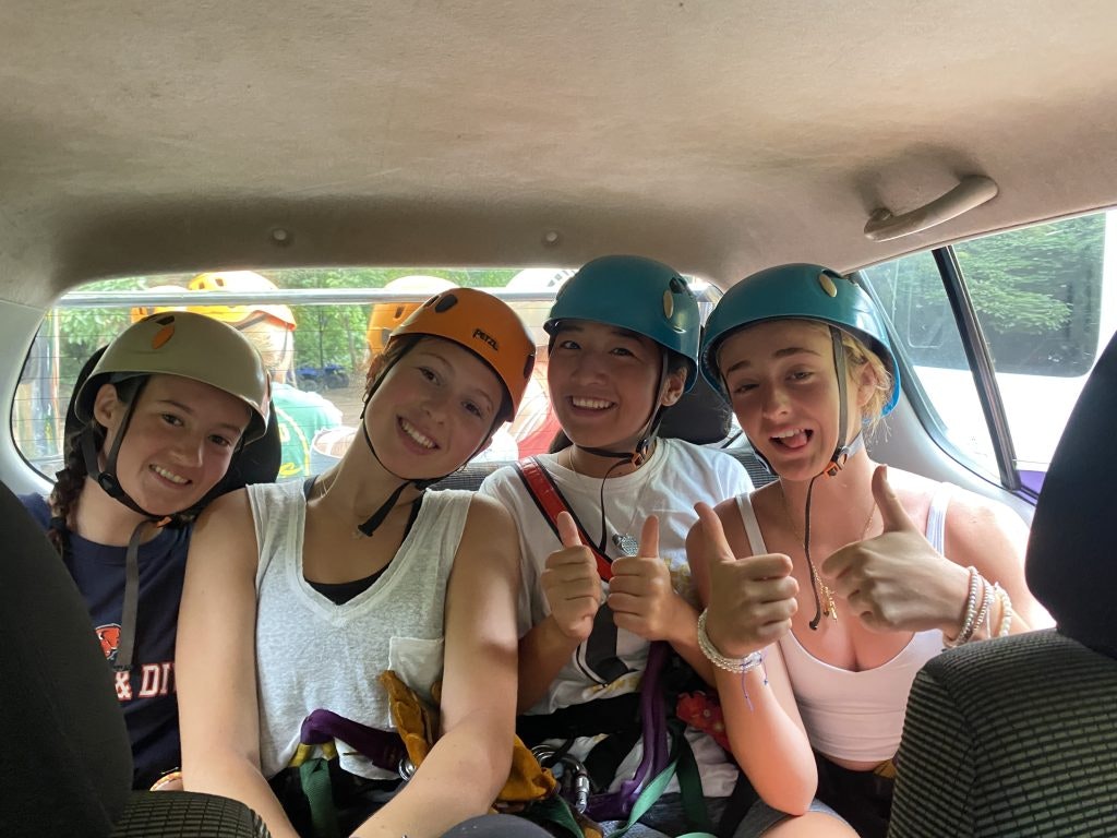 A group of students wearing hardhats in the back of a vehicle on their way to an adventure activity on an outdoor program.