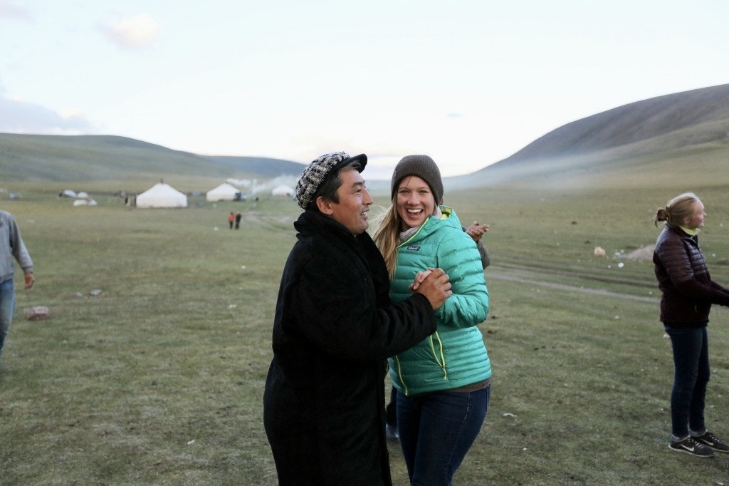 A summer program traveler dancing with a local Kazakh man at a ger camp on the Mongolian steppe at dusk