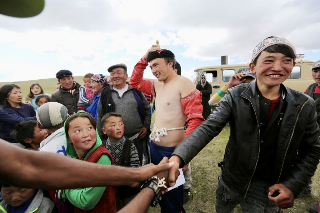 A young Mongolian wrestler in traditional dress greeting the crowd after a bokh match at a local Naadam festival