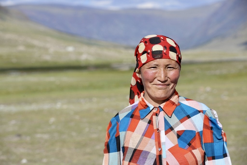 Portrait of a Kazakh woman in a red polka-dot headscarf and colorful plaid shirt on the open Mongolian steppe