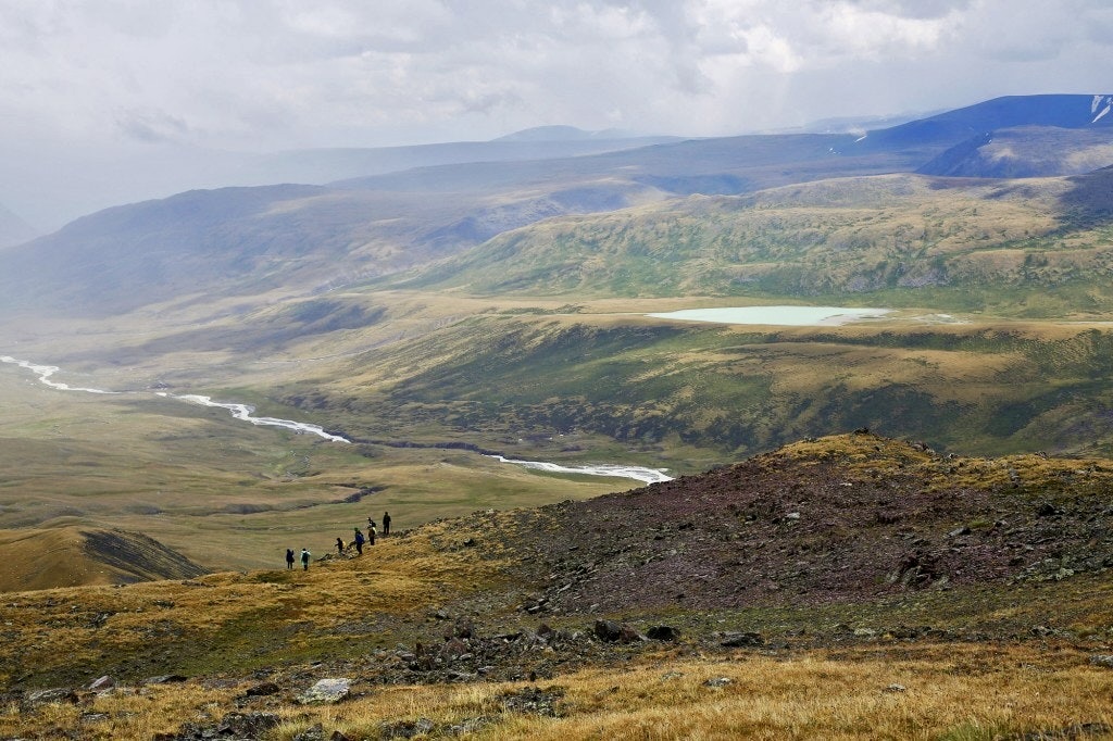 High school students trekking along a ridge above a glacial river valley and lake in Mongolia's Altai Mountains