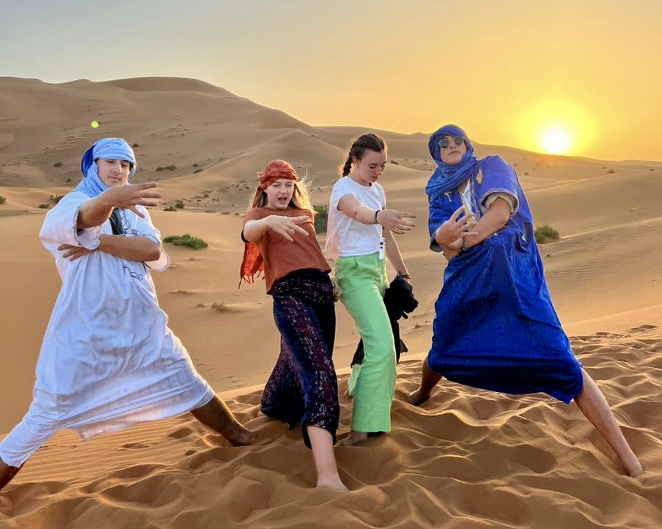 High school students in Berber robes and turbans posing on Sahara sand dunes at sunset in Morocco
