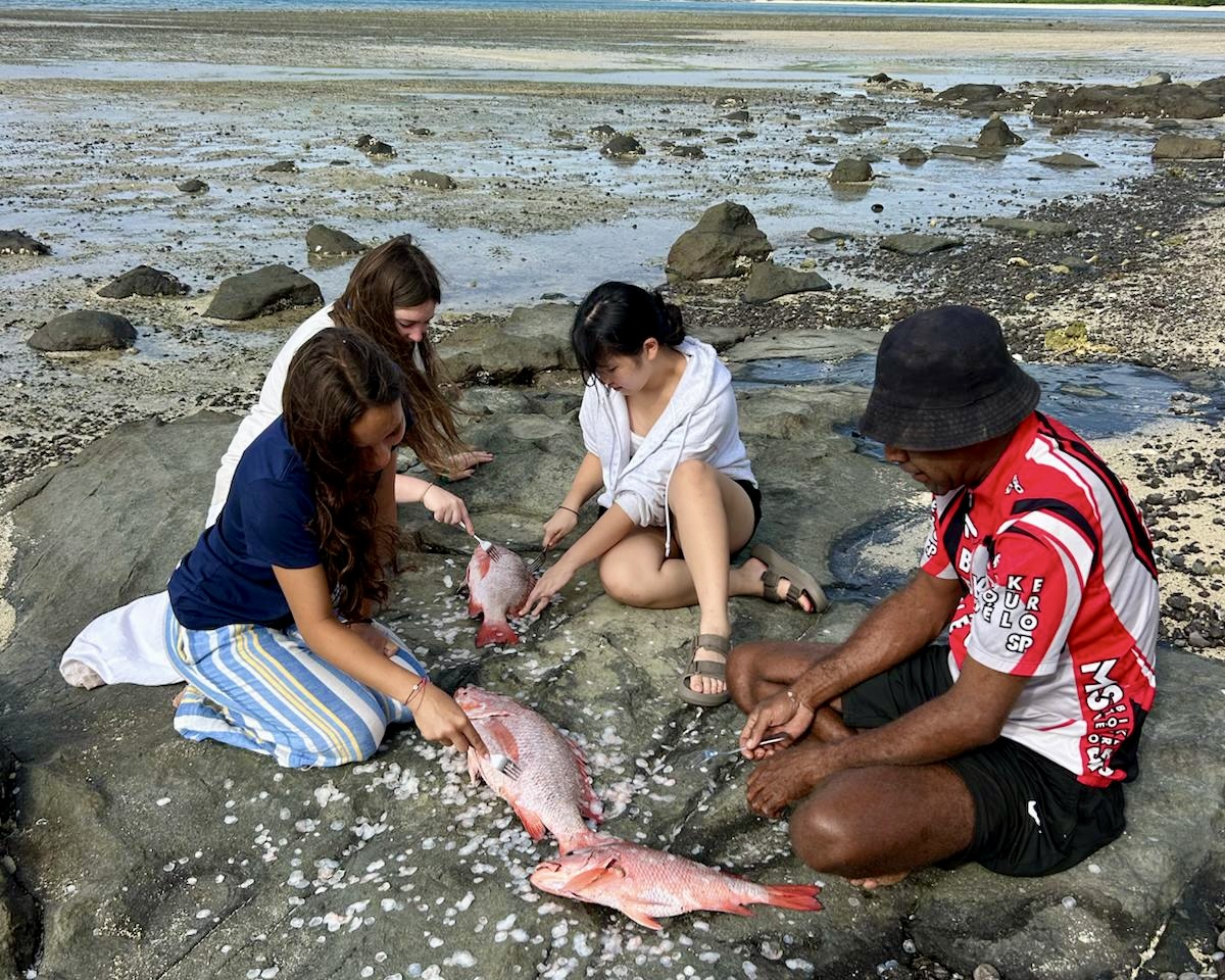 Fiji summer program students cleaning freshly caught reef fish with a local Fijian guide on the rocks at low tide