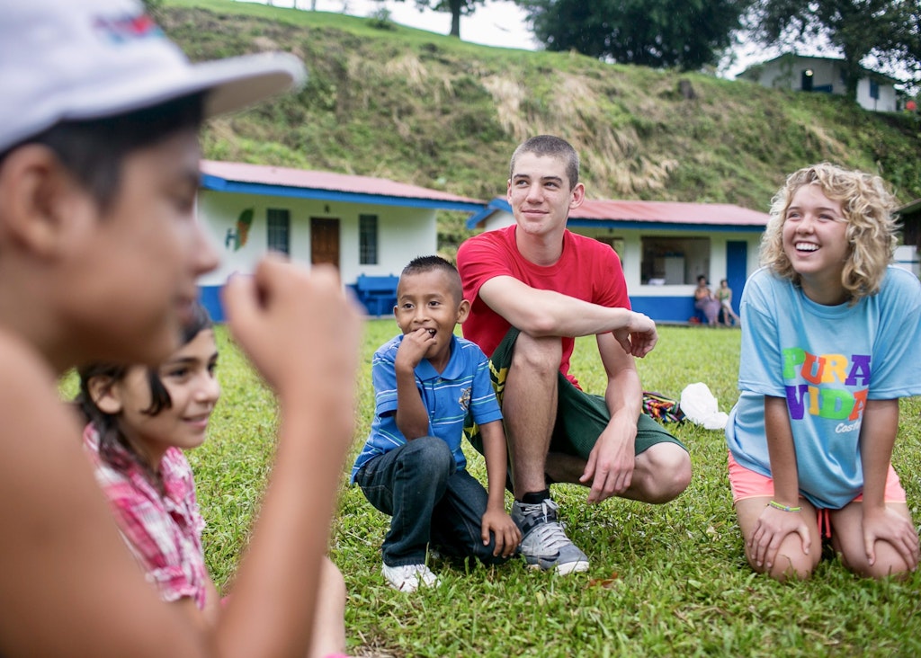 Teen and children sitting in a circle and smiling while at a summer volunteering leadership camp in Costa Rica.