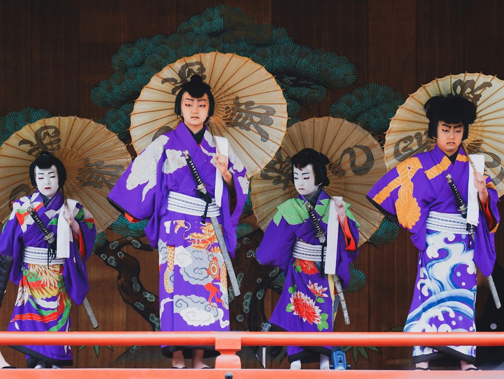 Young children wearing purple yukata and stage makeup give a kabuki performance.