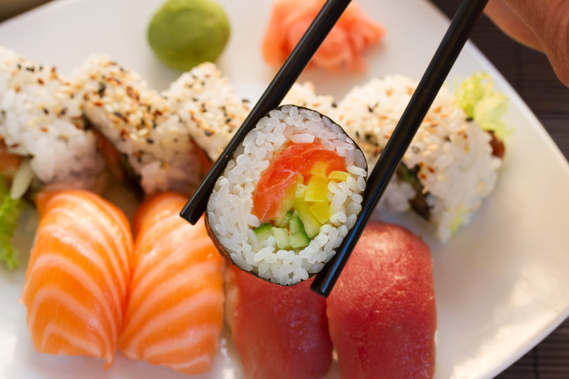 Chopsticks lift a sushi roll from a plate of nigiri and rolls