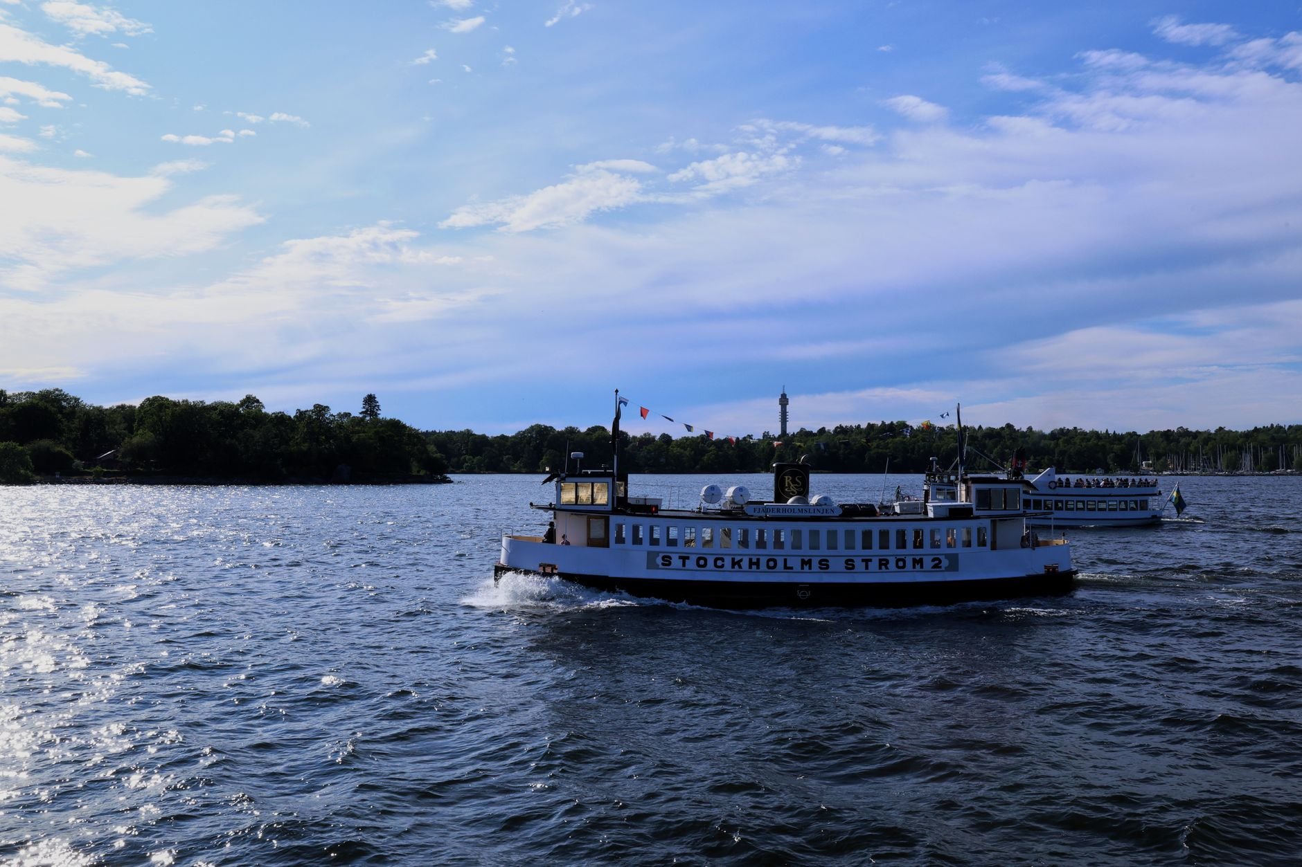 A white sightseeing boat crosses open water in central Stockholm on a clear day.