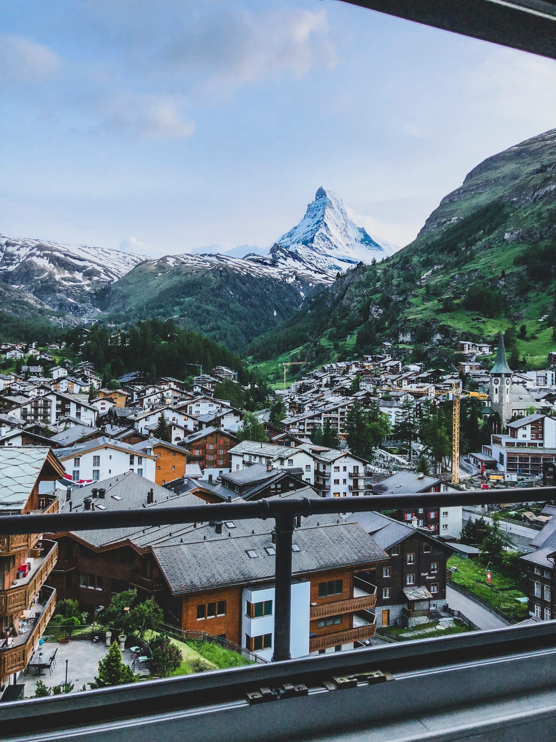 Chalets and slate roofs fill a valley floor below the Matterhorn, seen from a window above the village.