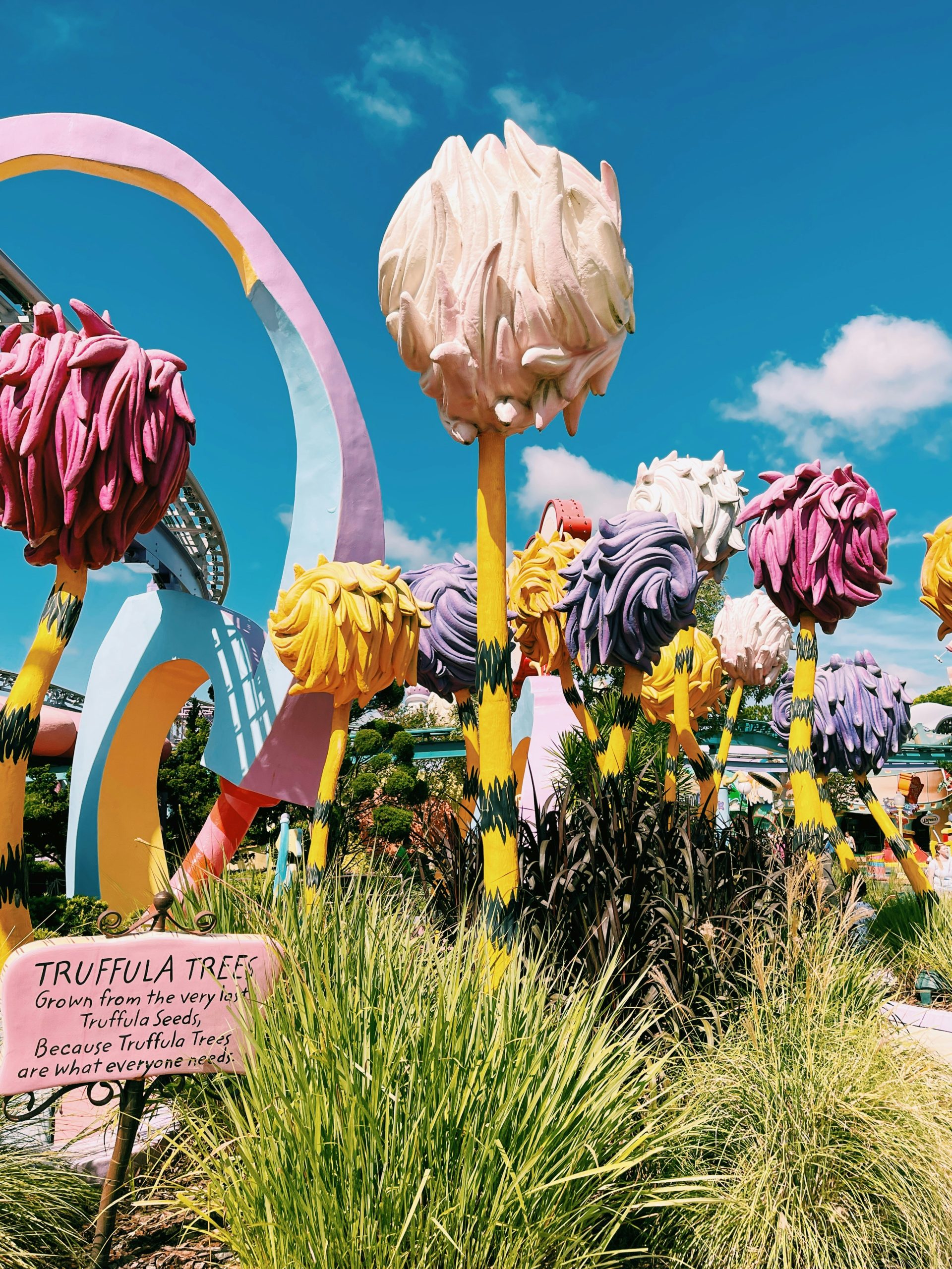 Colorful, cartoonish trees with yellow trunks and fluffy tops fill a vibrant outdoor setting. The imaginative scene evokes quotes about service learning, creativity, and shaping a better world.