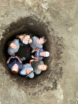 A group of students looks up from inside a deep hole, smiling and posing for the camera, during a teen travel program to Ecuador