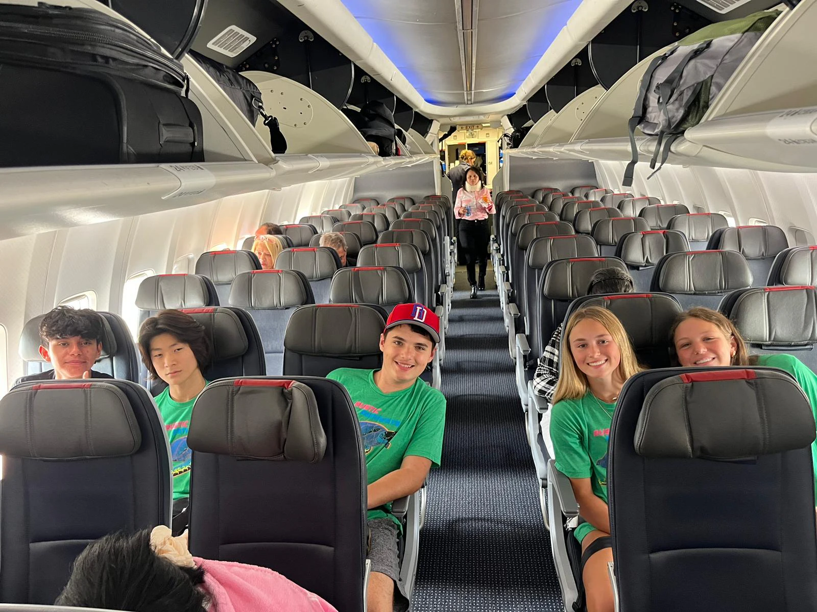 Rustic Pathways students in matching green shirts sit together on a chaperoned group flight