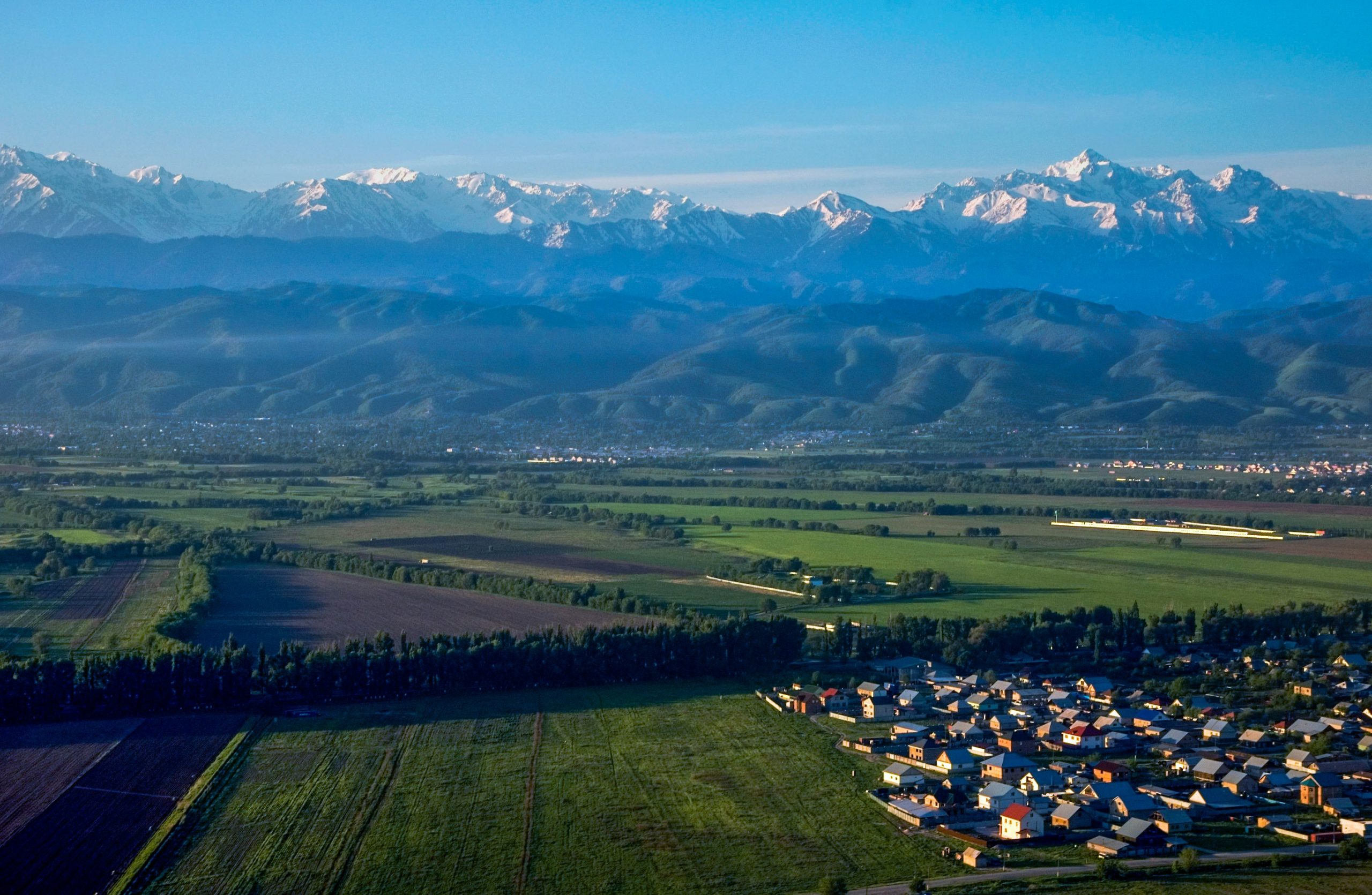 Snow-capped mountains rise above a green valley town on the outskirts of Almaty