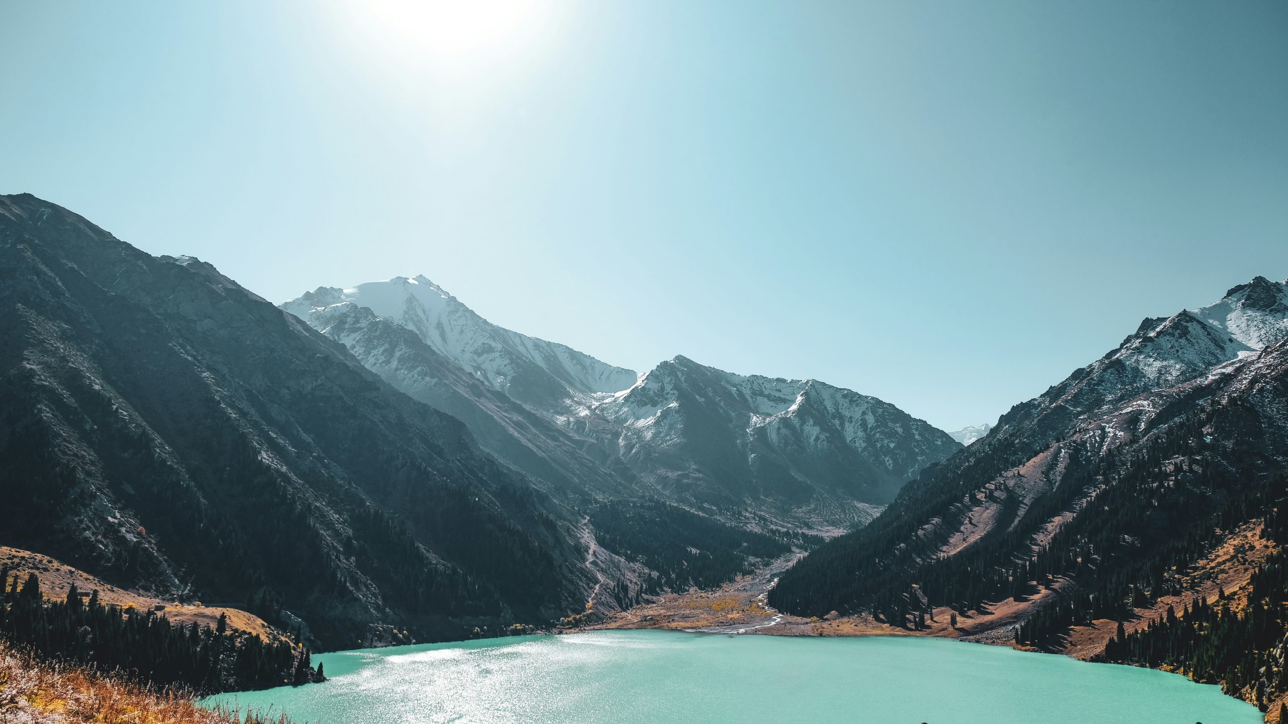 Students pause by a turquoise alpine lake ringed by snow-dusted mountains under a bright sky