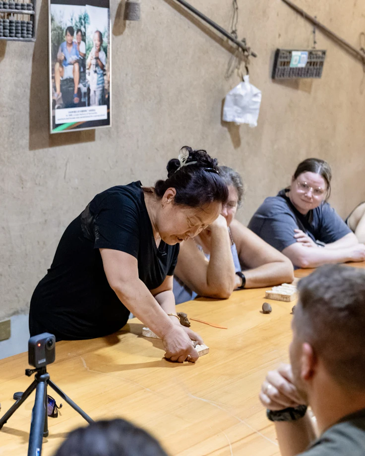 Travelers watch a craftswoman demonstrate miniature terracotta warrior making around a wooden table in China