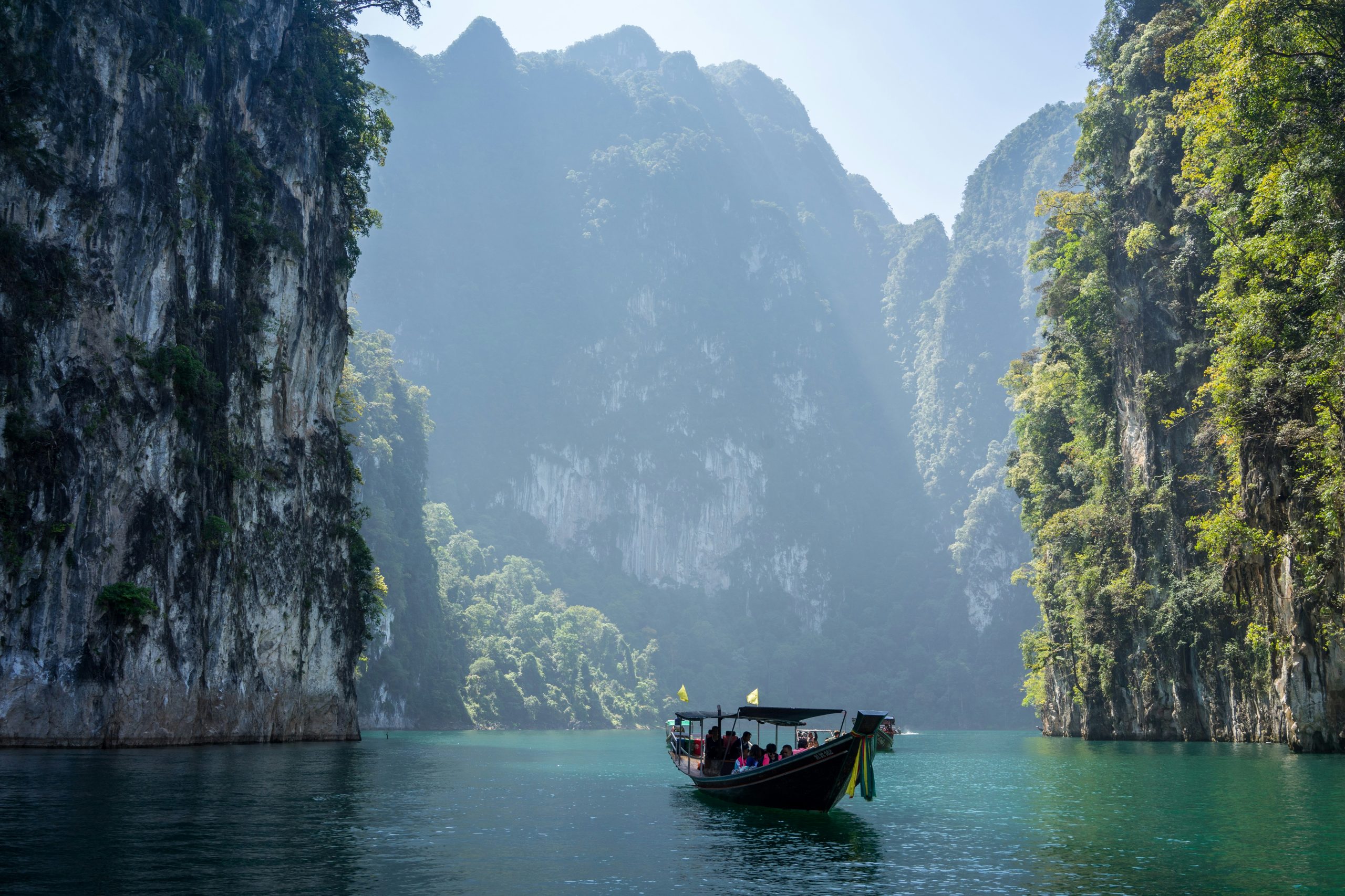 Picture of boat in ocean and tall mountains in the background in Khlong Sok, Thailand.