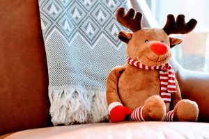 A stuffed toy of Rudolph the Red-nosed Reindeer sits on a sofa.
