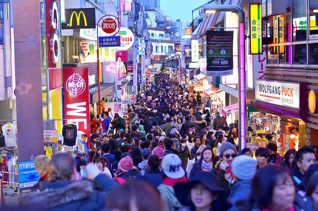 Crowds fill a neon-lit shopping street in Tokyo at dusk
