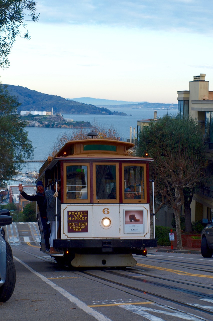 A cable car descends a San Francisco hill with the bay and Alcatraz Island in the background