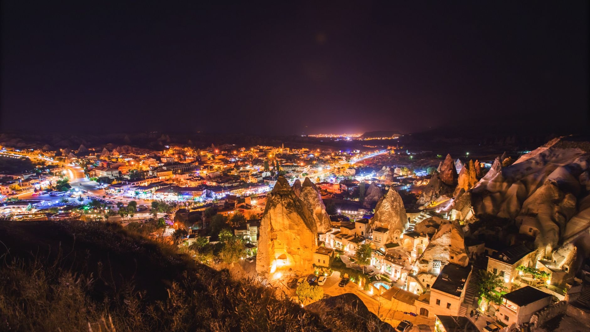 A valley town lit up at night, with lights tracing the cave dwellings built into the rock.