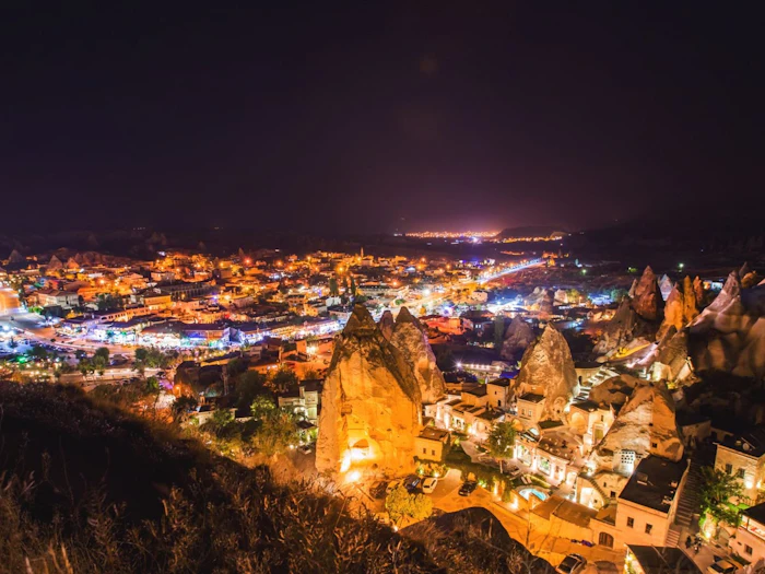 A valley town lit up at night, with lights tracing the cave dwellings built into the rock.