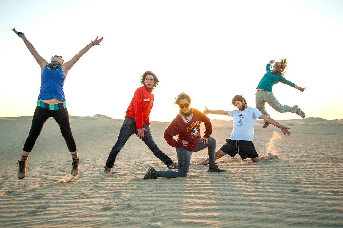 Group of gap year students jumping and posing playfully in a desert landscape at sunset