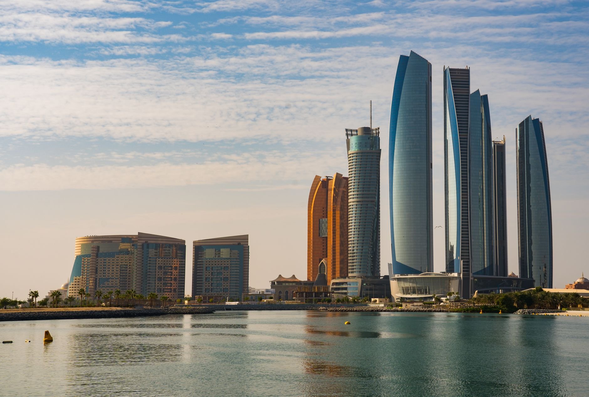 A skyline seen across the water, with the curved glass towers of a waterfront hotel and office complex catching the morning light.