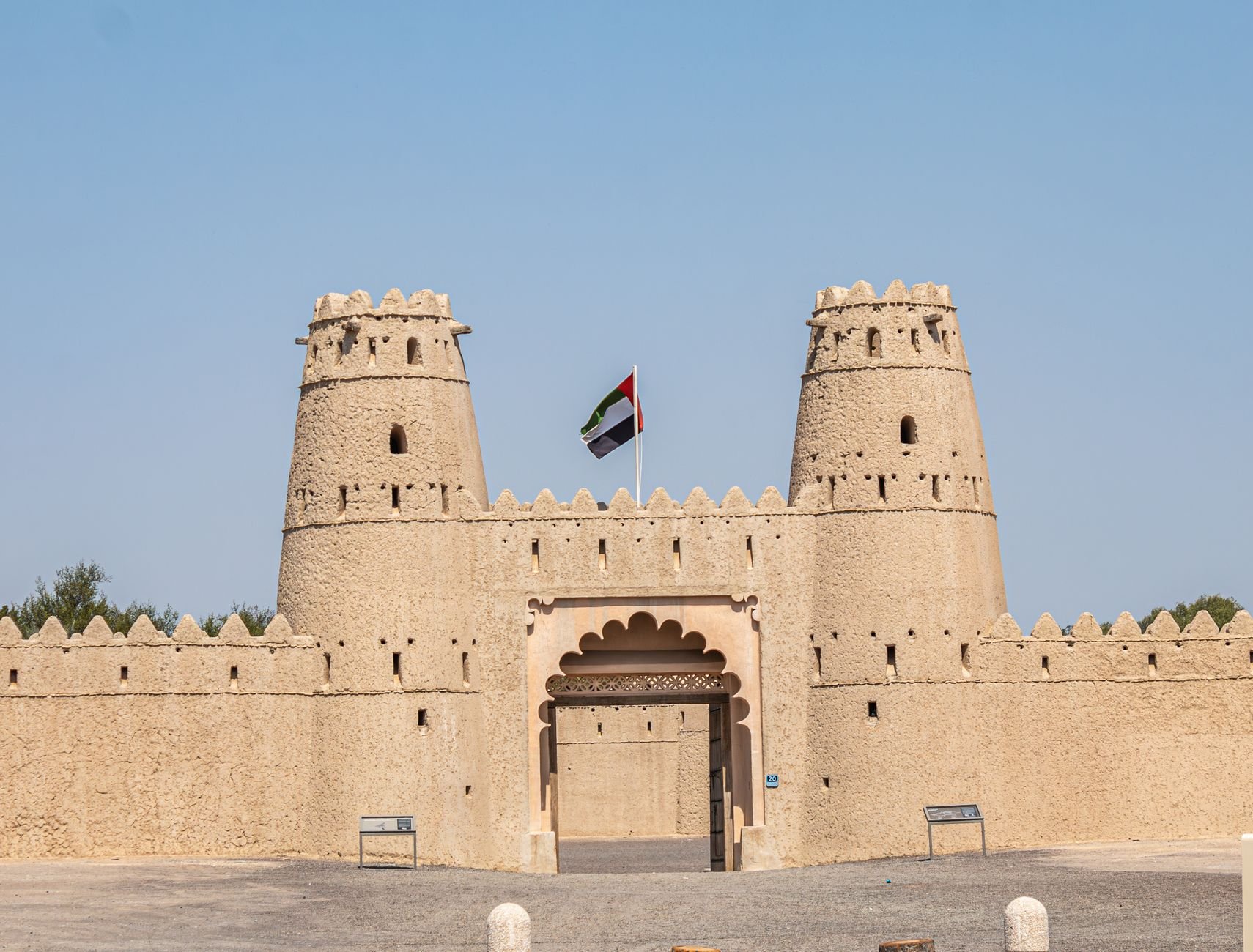The twin round towers and arched gate of a restored fort, with the national flag flying above the entrance.