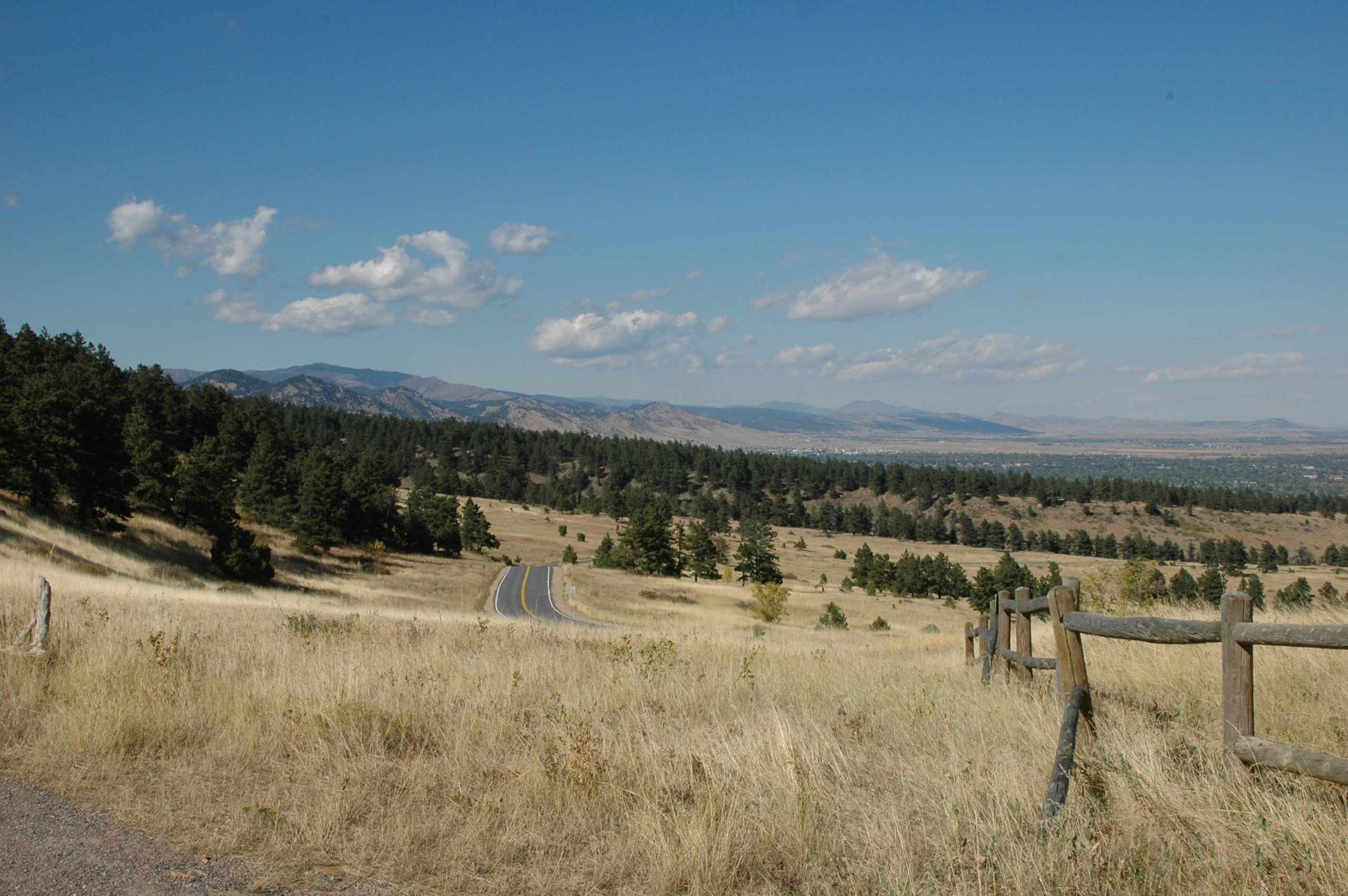 A road winds through grassy foothills toward distant mountains under a blue sky
